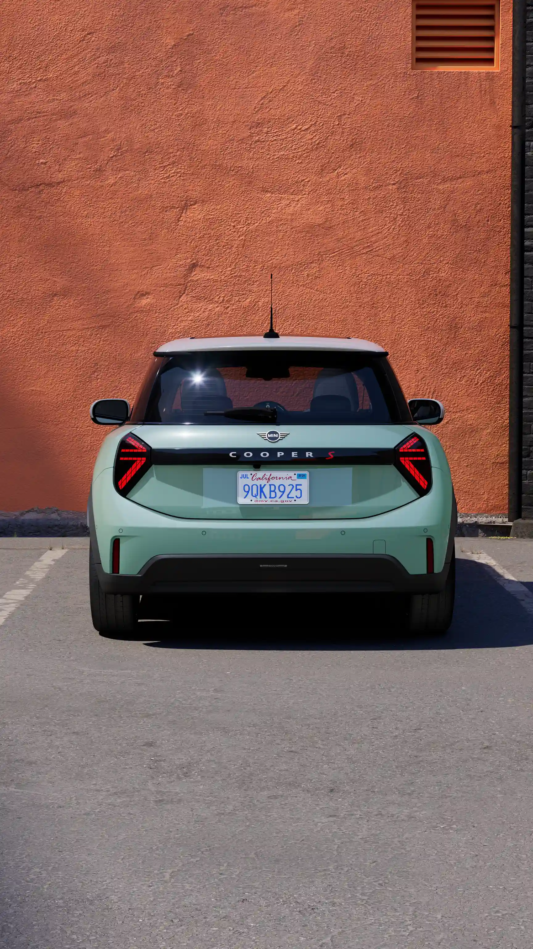 Rear view of a MINI Cooper S in Icy Sunshine Blue parked in a marked parking space against an orange wall.