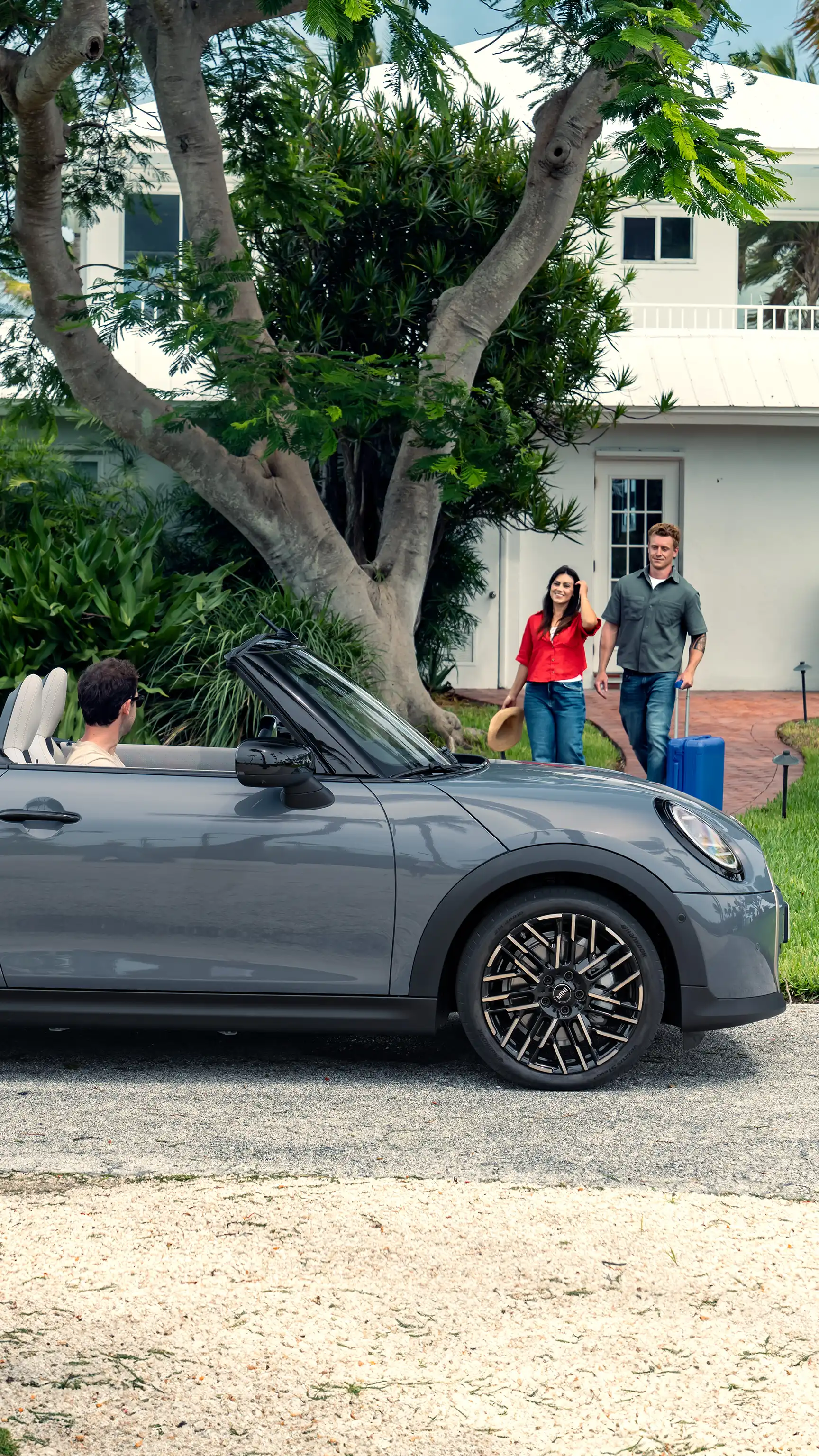 MINI Convertible parked in front of a house as two people walk toward it carrying bags.
