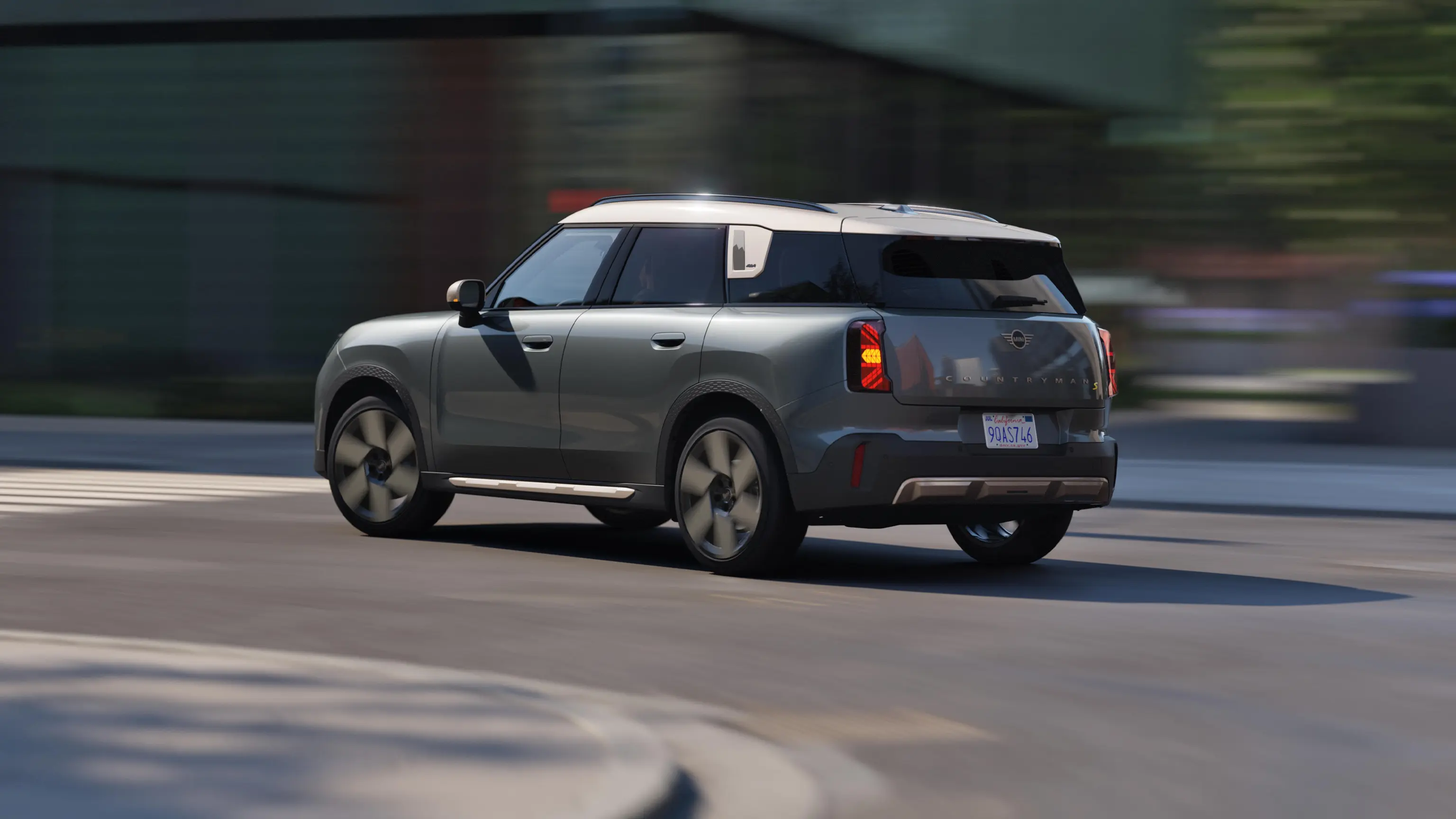 Rear three‑quarter view of a MINI Countryman in Slate Grey Metallic driving through an urban intersection.