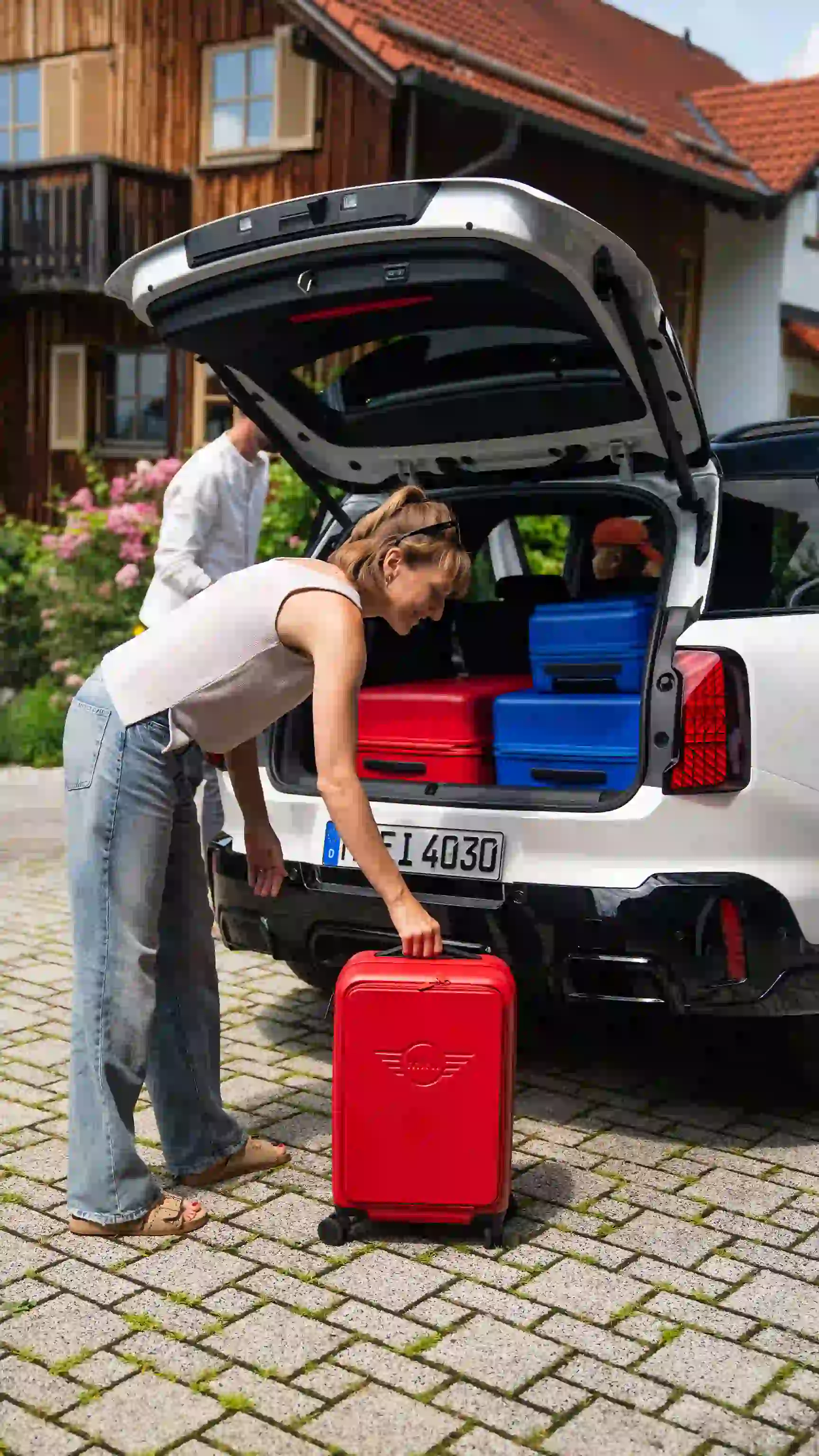 Person loading a red suitcase into the boot of a MINI Countryman in Nanuq White Metallic, packed with blue and red luggage.