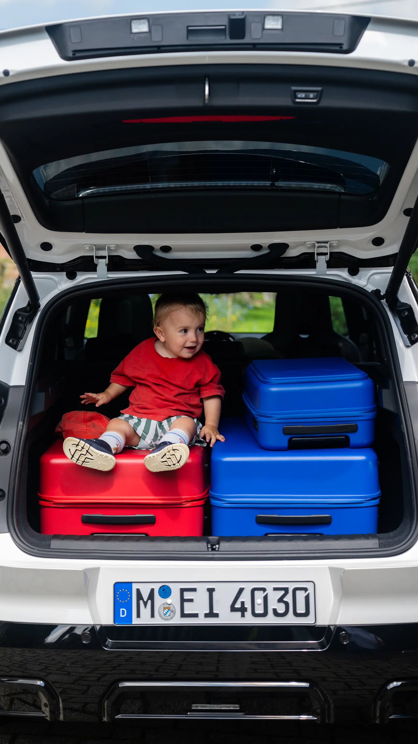 Child sitting on stacked suitcases in the open boot of a MINI vehicle.